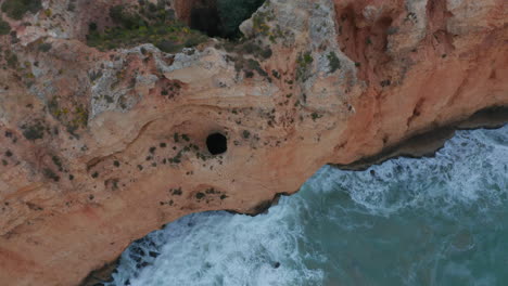 Aerial-drone-birds-eye-overhead-top-down-view-of-amazing-Lagos-Atlantic-coastline-with-waves-foam-crashing-against-cliff,-Portugal,-day