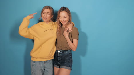 two happy friends posing in front of a blue background