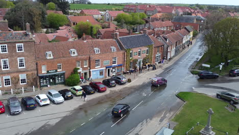 Toma-Aérea-De-Drones-De-Una-Furgoneta-Morada-Y-Un-Coche-Negro-Conduciendo-Por-Una-Carretera-Inundada-En-El-Mercado-De-Burnham,-Norte-De-Norfolk,-Reino-Unido