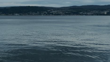 view of a town across calm water with hills in the background