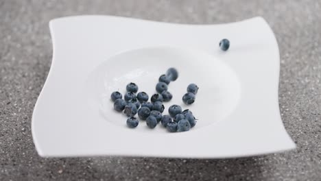 close-up of ripe, organic blueberries cascading into a stylish white bowl on a grey surface, capturing the dynamic motion of healthy food preparation.
