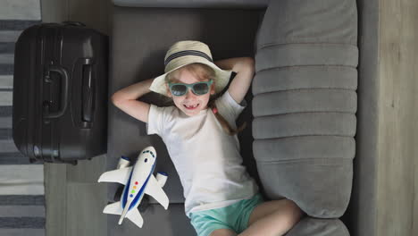 Toothless-girl-in-sunglasses-rests-on-sofa-near-airplane