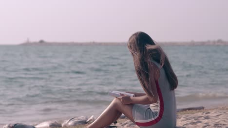 young-woman-with-long-hair-sits-on-beach-and-reads-book