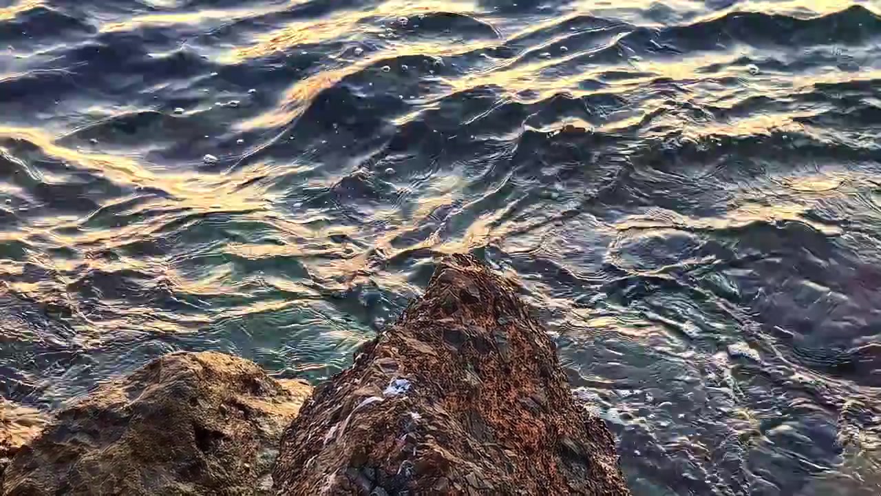 Nærbilde av krusninger i sjøvannet ved steiner langs strandkanten under solnedgang