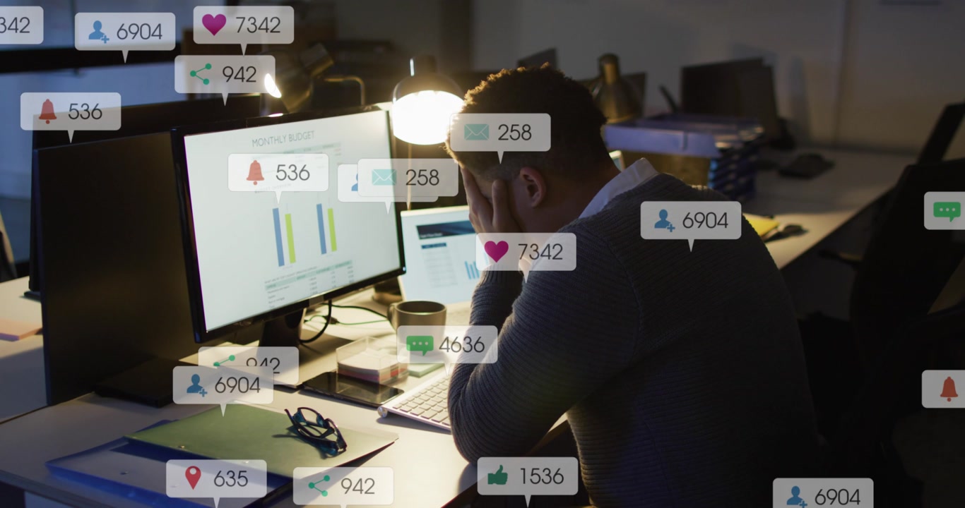 Man reading marketing charts at desk, alerts flooding monitor causing stress while tracking KPIs