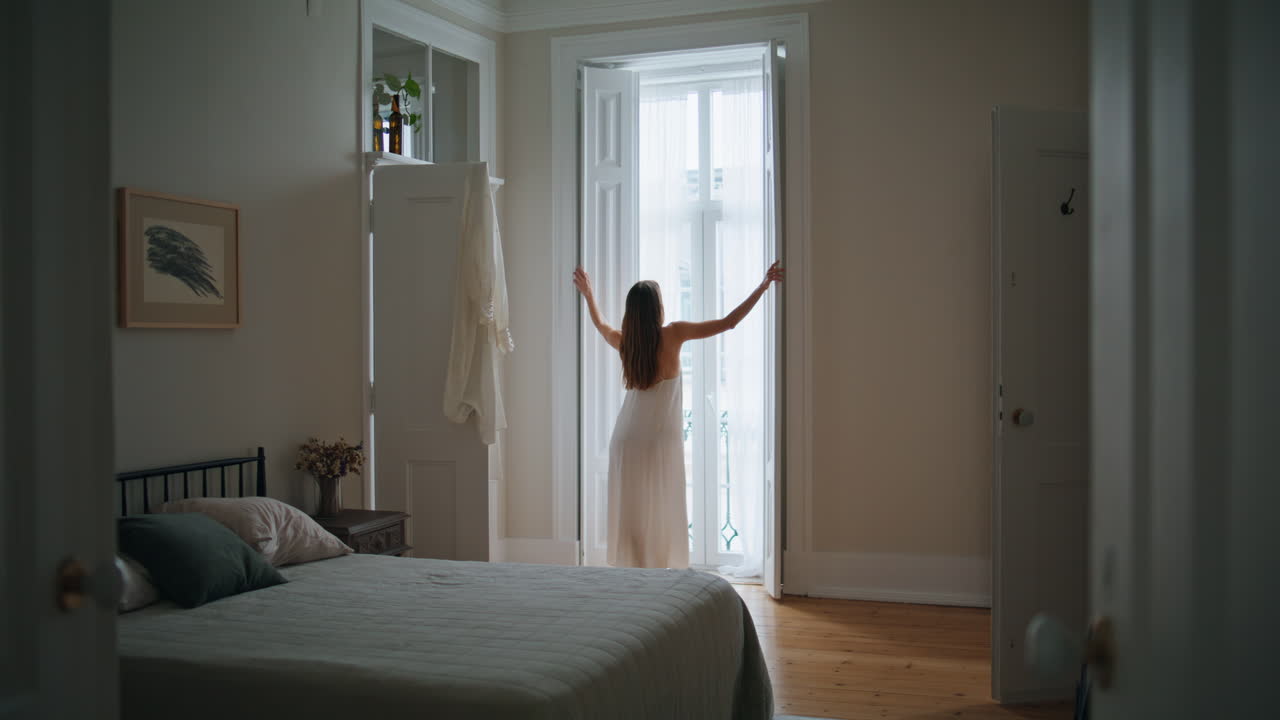 Young woman opening blinds home morning. Relaxed girl looking window back view