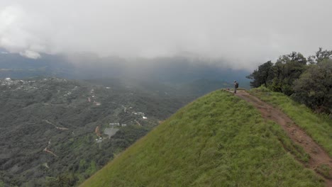 4k-Aerial-Reveal-Shot-of-a-25-year-old-Indian-Male-and-Shirui-Village-from-the-top-of-Shirui-Peak,-Ukurul,-Manipur,-India