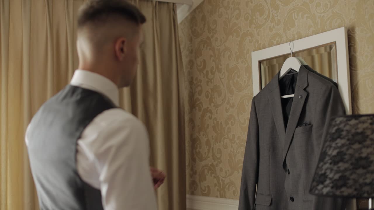 잘생긴 신랑 사업가가 집에서 회색 재을 입기 위해 준비하고 있습니다.