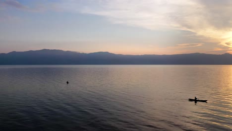 Aerial-view-over-man-rowing-boat-on-Lake-Toba-at-sunset-in-North-Sumatra,-Indonesia