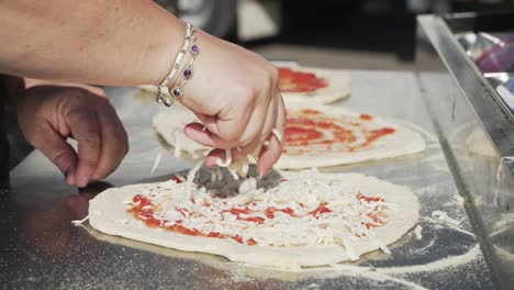 lady's hands spreading mozzarella cheese on raw pizza dough outdoors