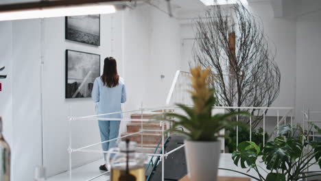 woman looking art paintings at home. thoughtful girl walking drinking beverage