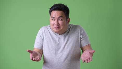 young handsome overweight asian man against green background