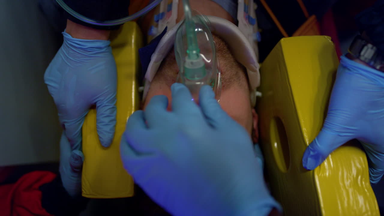 수갑을 입은 구급대원들이 산소 마스크를 입은 피해자에게 구급차로 도움을 주고 있습니다.