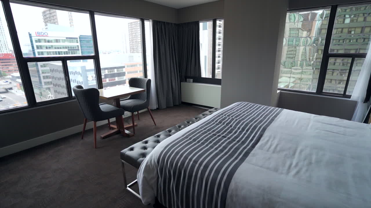 A spacious and elegantly designed hotel room with a king-sized bed draped in plush linens and adorned with pillows and a cozy blanket