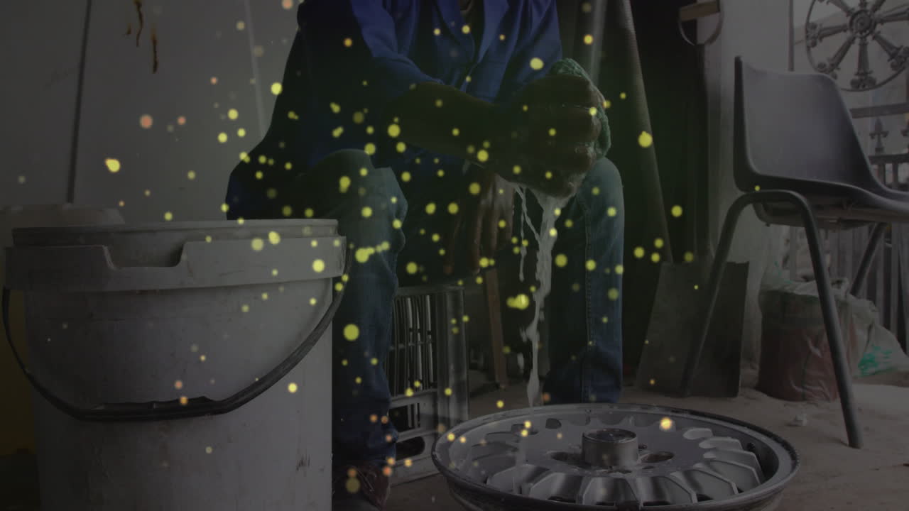 Male mechanic cleaning car wheel rim in auto garage, with animated soap suds and data overlay