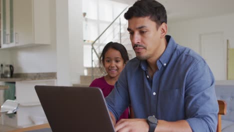 Happy-hispanic-father-and-daughter-sitting-at-table-looking-at-laptop