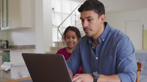 Feliz-Padre-E-Hija-Hispanos-Sentados-En-La-Mesa-Mirando-La-Computadora-Portátil