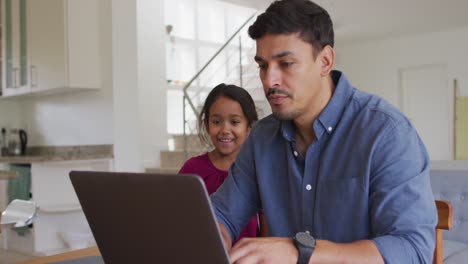 padre y hija hispanos felices sentados en la mesa mirando la computadora portátil