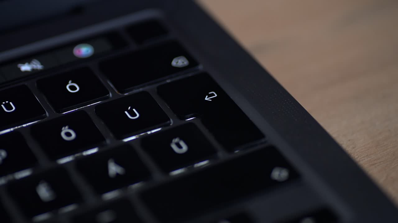 A close-up shot of a person's finger about to press the enter key on a backlit laptop keyboard. The keyboard features accented characters, indicating an international layout