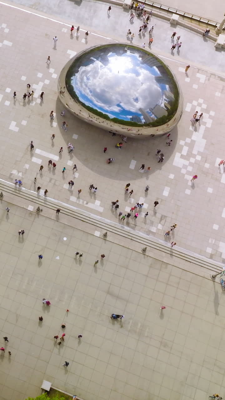 Chicago Bean in the middle of the square surrounded by greenery. Sky and skyscrapers reflecting in the Cloud Gate. Aerial view. Vertical video