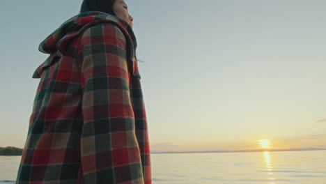young woman standing by lakeside with lantern, watching picturesque sunset