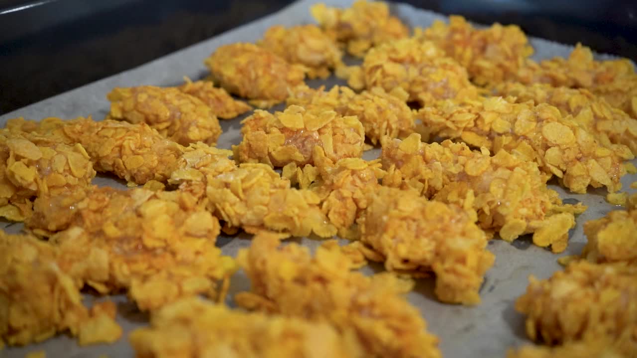 pollo crudo cubierto de copos de maíz en una bandeja para hornear