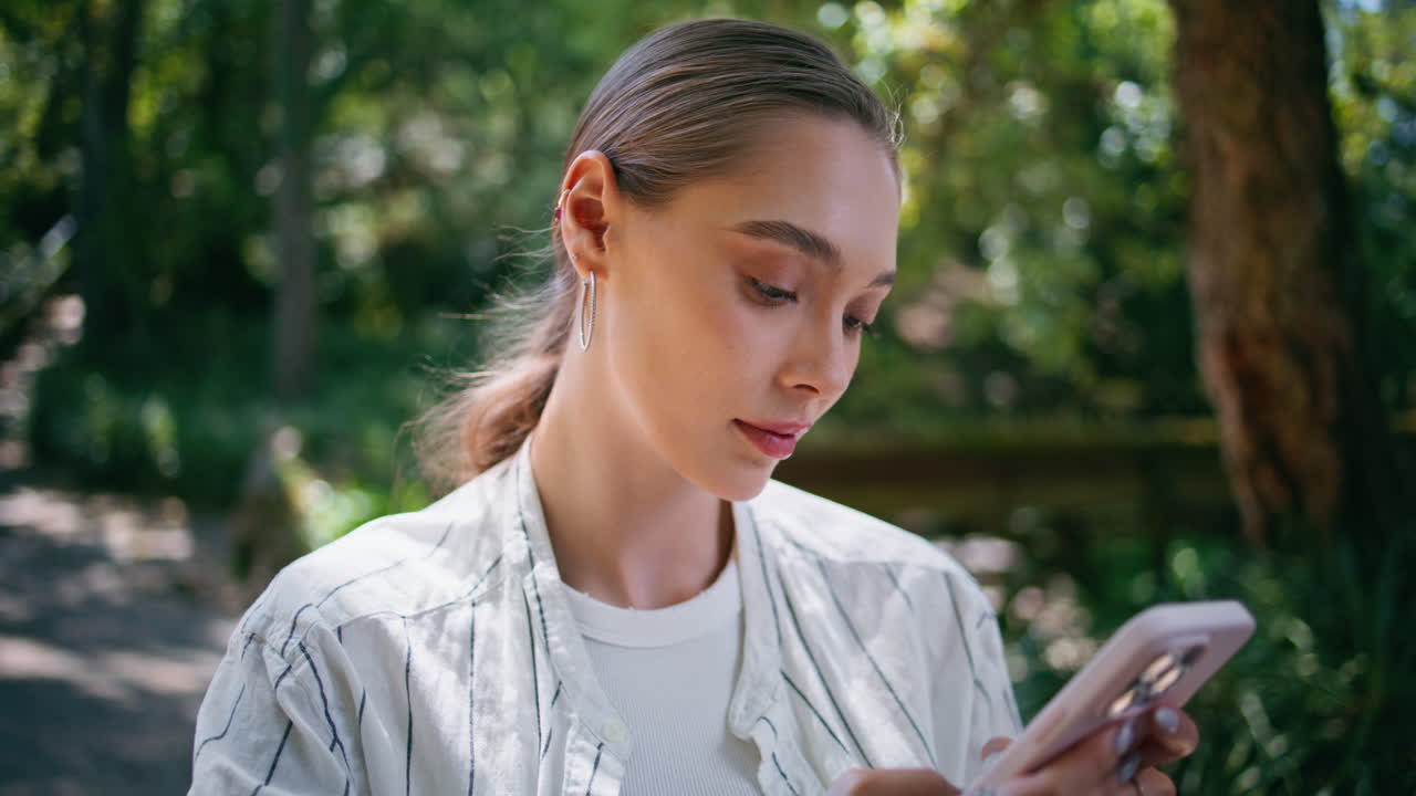 휴대전화를 입력하는 사려 깊은 여성, 가까이 서 있는 숲, 문자 메시지를 보내는 젊은 여성