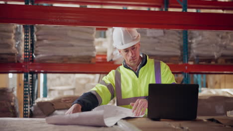 warehouse worker reviewing blueprints with laptop