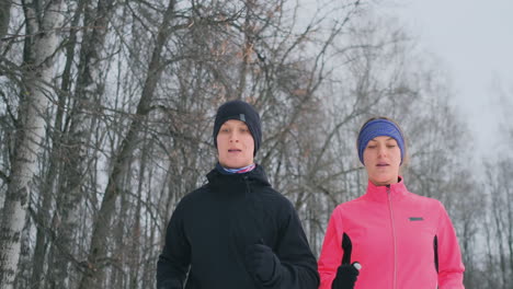 una pareja joven y saludable positiva corriendo con ropa deportiva por el bosque en la mañana de invierno