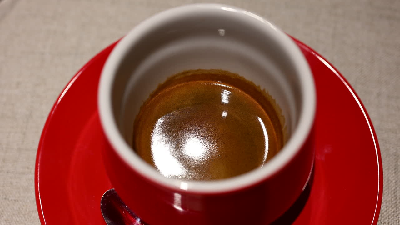 Caffè espresso fresco servito in una tazza di ceramica rossa con crema in superficie, in un ambiente da bar