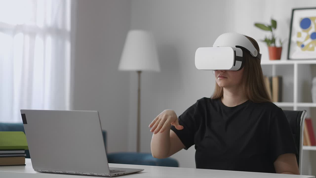 young female user is viewing screen of laptop by modern vr head-mounted display, gesticulating by hands for control