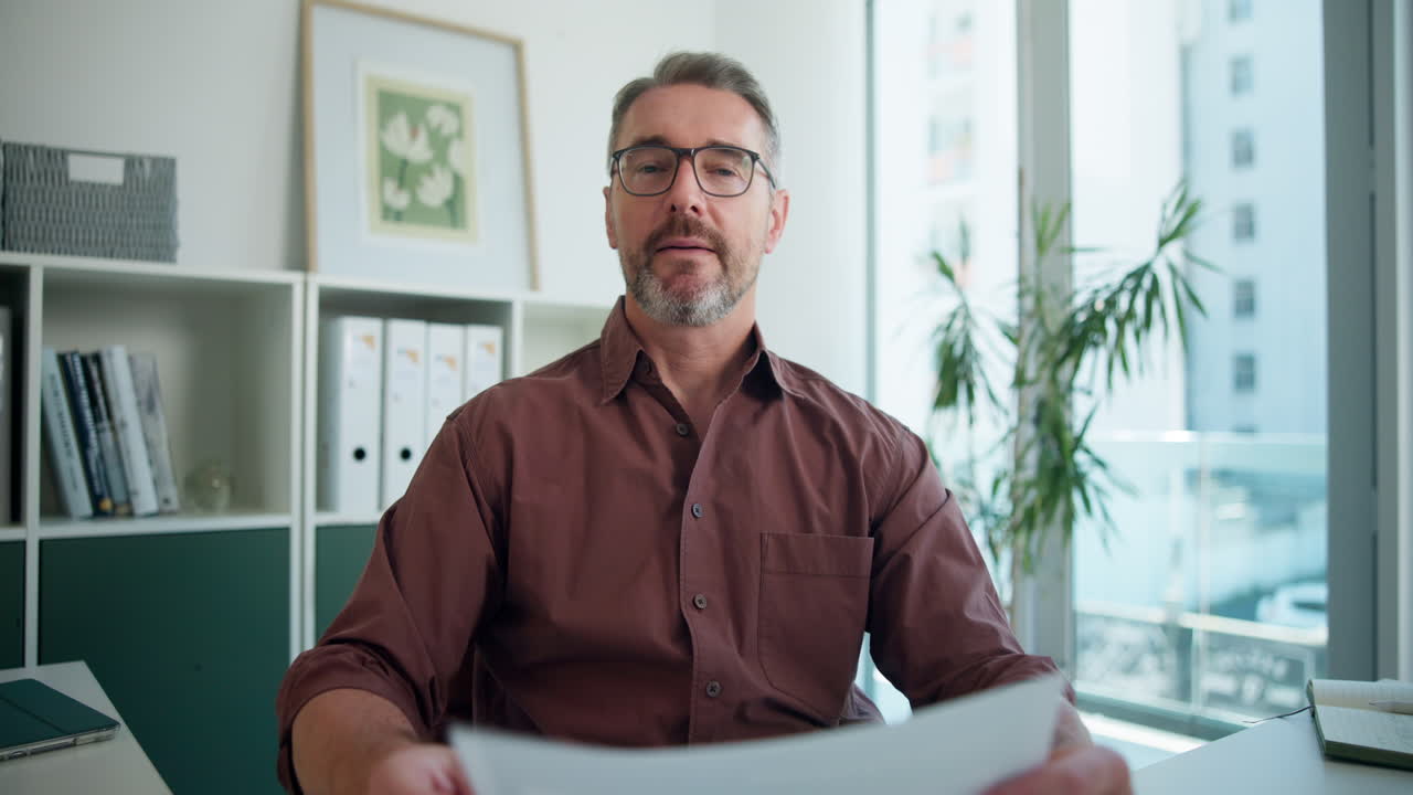 Professionel mand i videoopkald holder dokumenter på kontoret