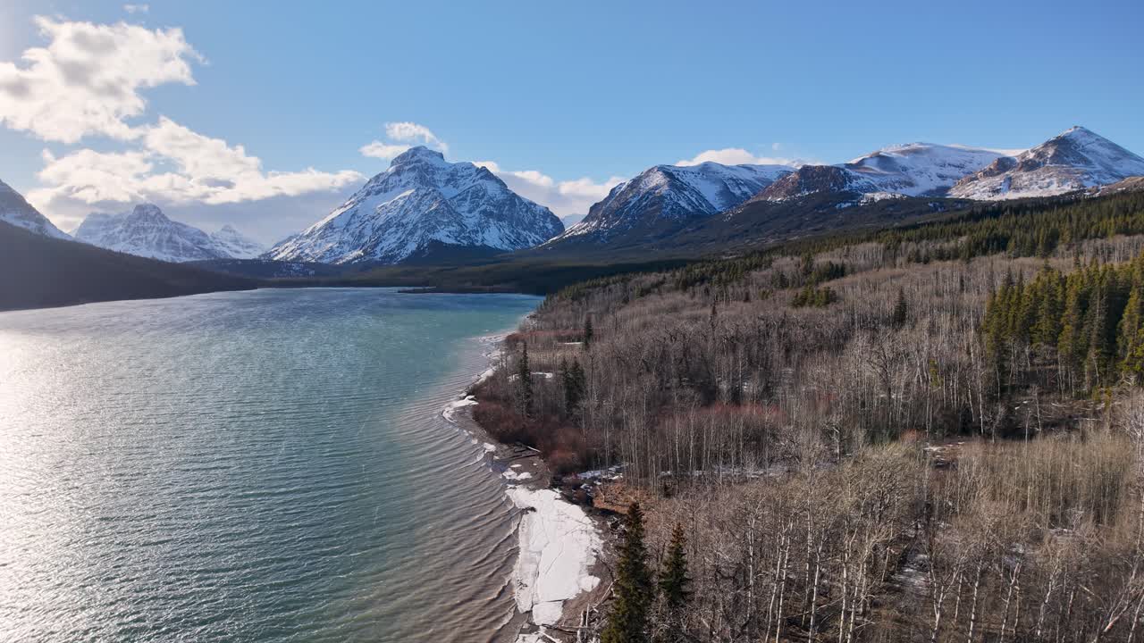Vista aerea di un lago incontaminato e della sua riva con montagne innevate e foreste di conifere nel Montana