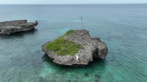 Sculpture-of-person-climbing-on-rock-in-middle-of-sea,-Playa-Caleton-beach,-Rio-San-Juan-in-Dominican-Republic