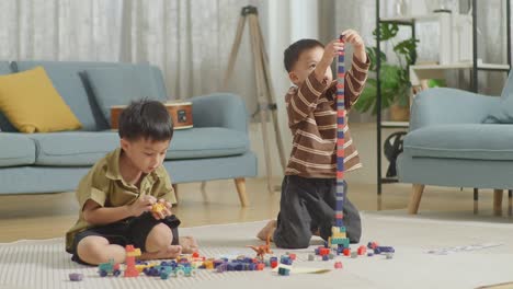 full body of asian kids assemble the construction set colorful plastic toy brick on a mat at home