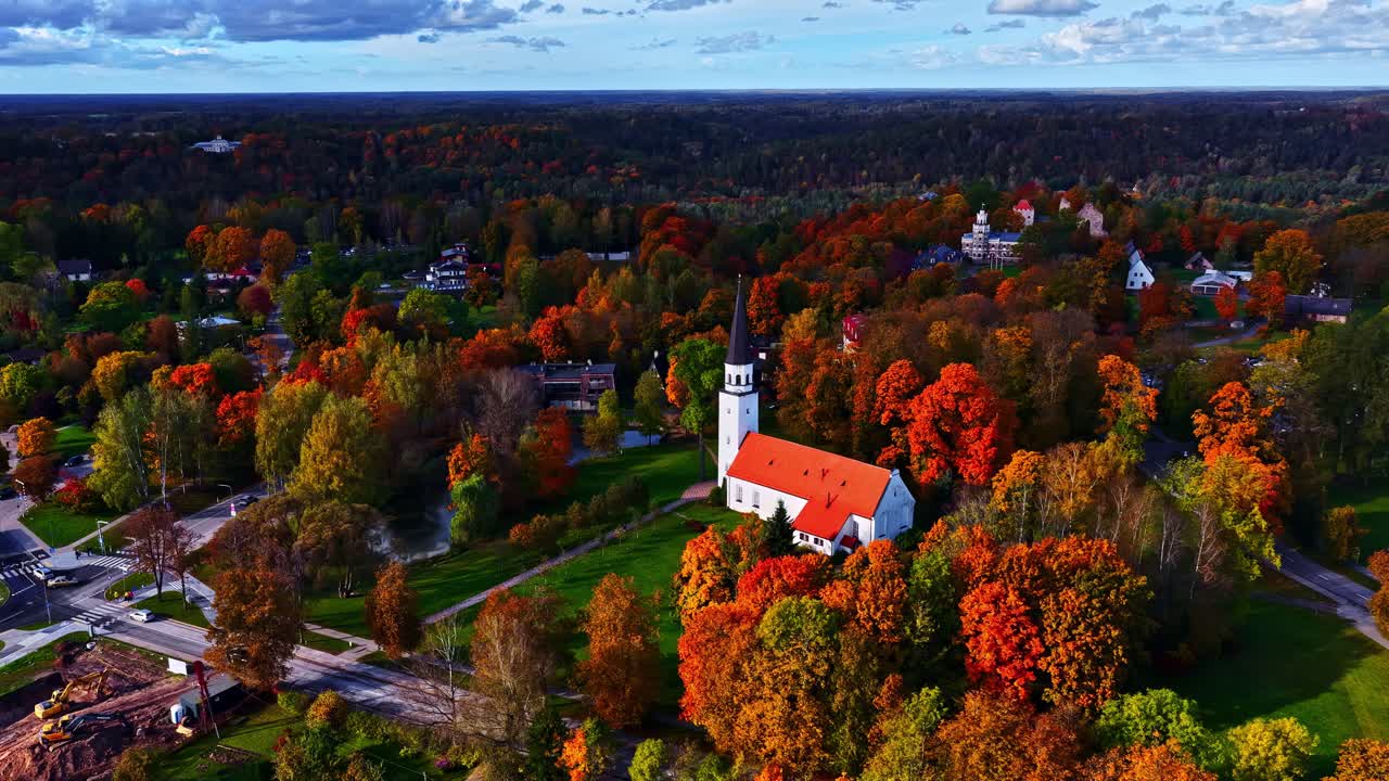 Aerial pullback of autumn countryside with orange trees and small white and orange roof church nestled in forest