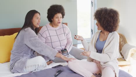 happy diverse female friends doing make up and smiling in bedroom