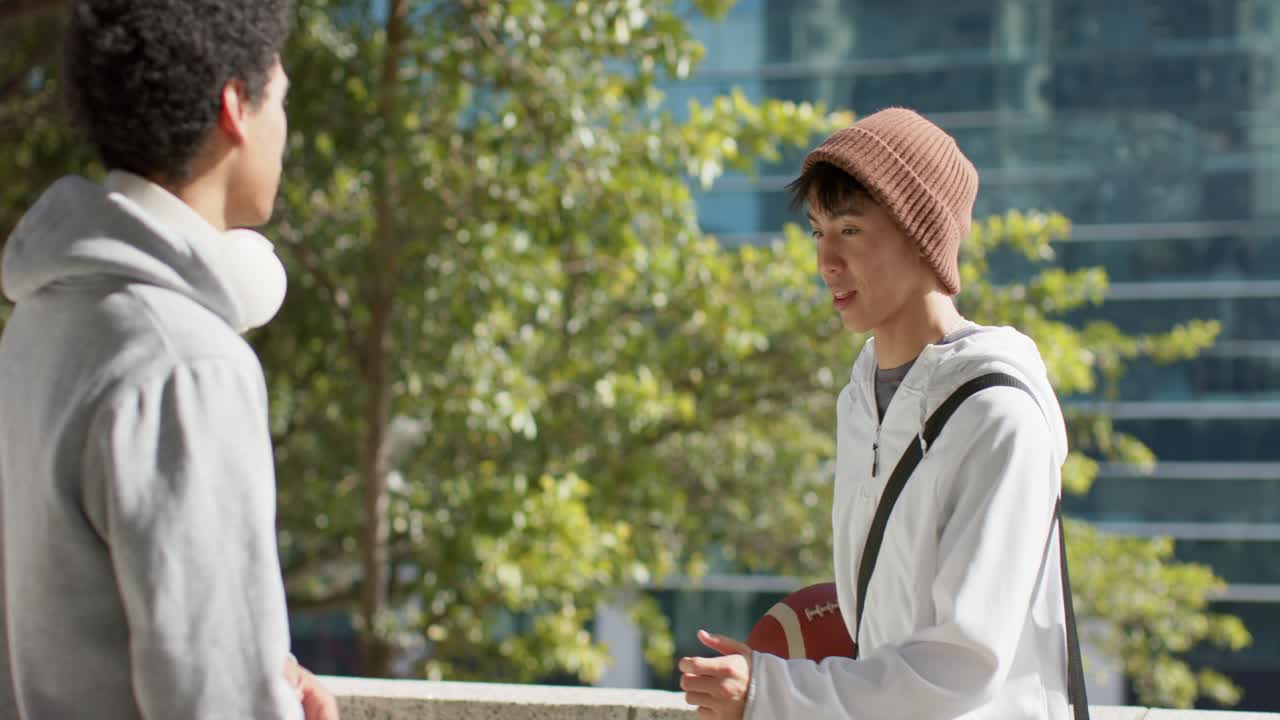 都会の広場でフットボールをパスする多様な男性の友人たちが、アッと驚くキャッチと笑いを巻き起こしています。