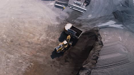 Drohnenvideo-Eines-Frontladers,-Der-Einen-Steintransporter-Mit-Zuschlagstoffen-Aus-Einer-Halde-In-Einem-Bergwerk-Belädt