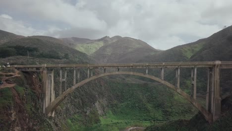 Aerial-drone-view-passing-underneath-South-Pacific-Highway-surrounded-by-lush-green-valley-mountain-scenery