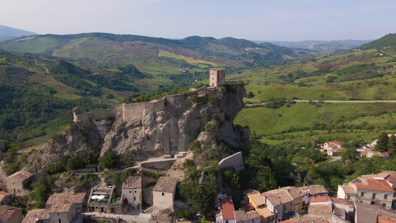 아래의 작은 마을을 드러내는 절벽 옆에 있는 중세 성에서 멀리 날아가는 드론 샷