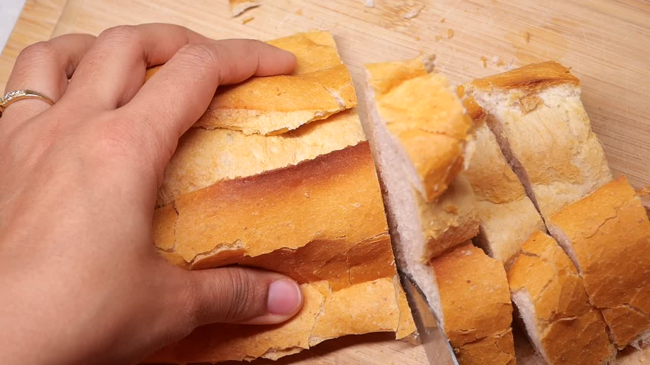 Hand Slicing Fresh Baguette on a Wooden Cutting Board