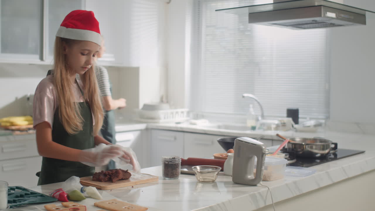 Girl Wearing Christmas Hat Making Chocolate Dough Helping Mother at Kitchen