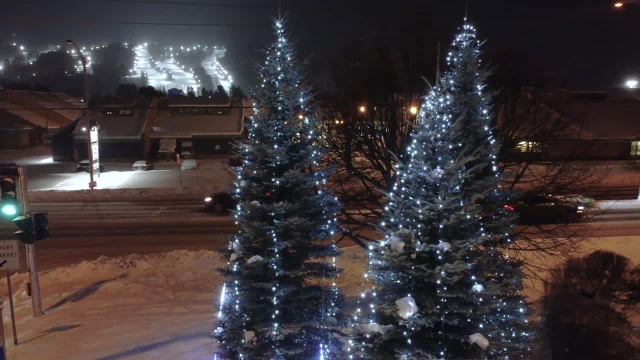 Parallax drone shot of Christmas fir trees illuminated with white lights during the night in Saint-Sauveur, Quebec, Canada