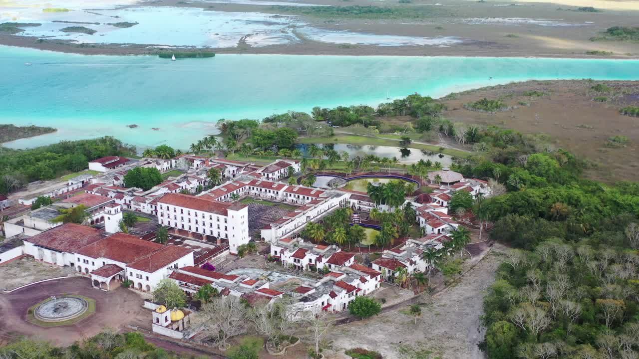 Ripresa aerea con drone dell'hotel fantasma abbandonato accanto alla Laguna dei Sette Colori a Bacalar, Messico. Rovine uniche circondate da acqua turchese, natura tropicale e scenari di viaggio iconici