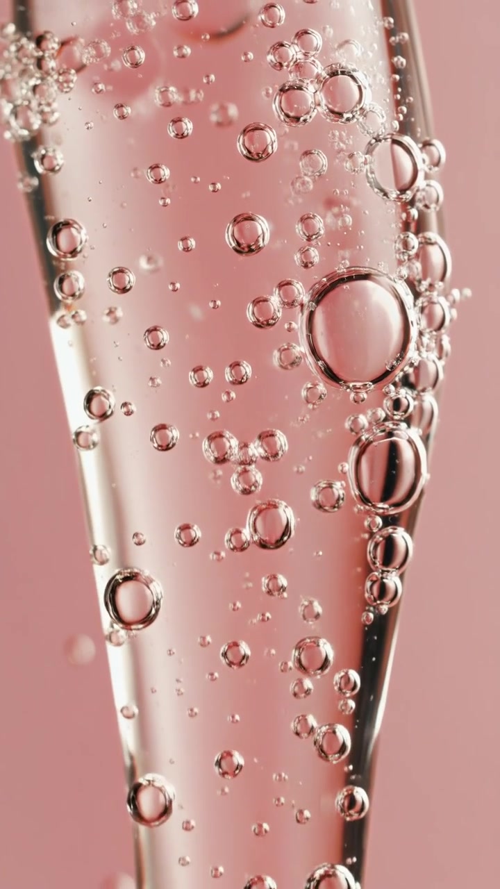 Macro ravvicinata di un siero in gel trasparente pieno di bolle d'aria all'interno di una pipetta di vetro su sfondo rosa