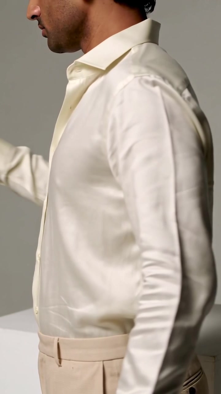 Video verticale: Modello che si sistema e si gira per mostrare la vestibilità di camicia e pantaloni in un set grigio su indicazione, con etichetta visibile.