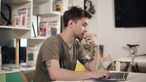 attractive male programmer at his 20's is laughing while typing something on laptop keyboard.