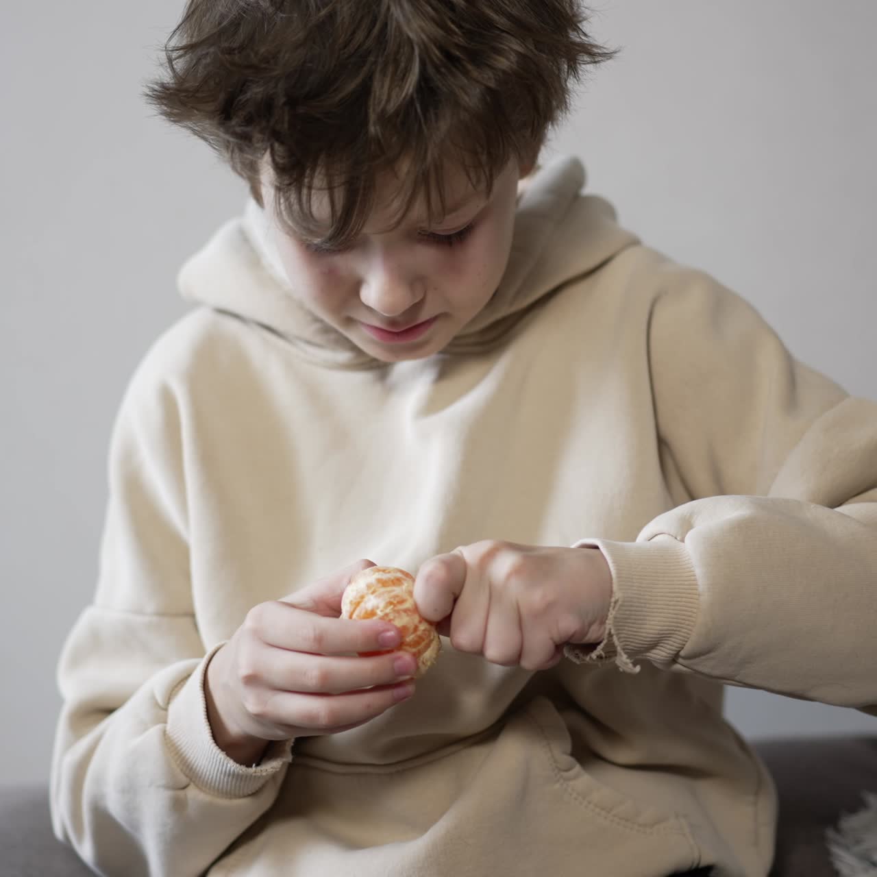 Calm Caucasian teenager peeling tangerine. Boy slowly peels the fruit and breaks it into pieces
