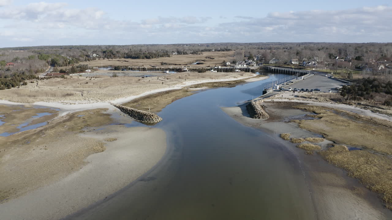 The camera pushes in towards the entrance of Rock Harbor in Orleans, Ma. You can see a group of people walking towards the small beach and the breakwater structures.